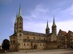 A stone cathedral with two towers on the west façade and two towers flanking the choir, all four towers are topped with slender, pointed metal roofs.