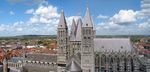 A grey stone cathedral with a central square tower flanked by 4 square towers. Surrounded by the red roofs of the old city.