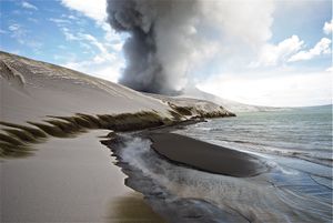 Grey ash dunes, shaped like sand dunes, at the ocean's edge.