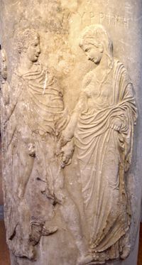 A carving of a noble robed man and woman apparently leading a demure, robed woman. The man's robe is open, exposing his penis. He holds the hand of the woman.