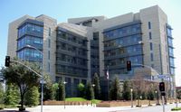 Exterior view of a beige building, composed largely of windows with several small trees in the foreground.