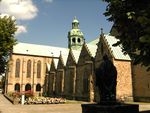 A romanesque stone cathedral, view of the side chapels and transept. The green copper dome over the transept crossing is visible.