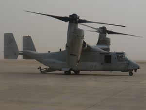 A side view of an MV-22 resting on sandy ground in Iraq during the day with its ramp lowered.