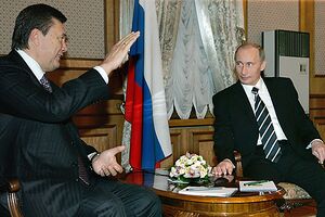 Two men in suits sit talking around a low wooden table.