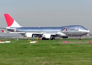 A Boeing 747-400F aircraft on the taxiway, with green grass strip in the foreground and grey sky in the background