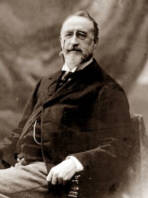 seated middle-aged white man, with medium-length moustache and neat beard, looking benignly towards the camera