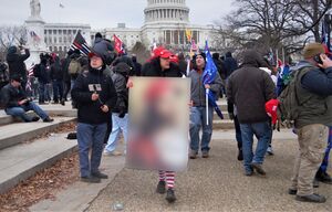 A Trump supporter carries a QAnon-tagged placard with Jesus wearing a MAGA hat at the moment the U.S. Congress was violently attacked by rioters on January 6, 2021. The placard is blurred for copyright reasons.