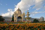 Large cream-coloured building with central dome and grand arched entrance, fronted by flowered gardens and a tiered fountain