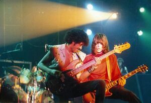 Phil Lynott plays bass guitar next to a guitarist