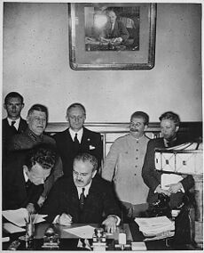 Soviet Foreign Minister Vyacheslav Molotov signs the Molotov–Ribbentrop Pact. Behind him stand German Foreign Minister Joachim von Ribbentrop and Soviet Premier Joseph Stalin.