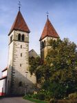 A grey and white stone church with two square towers, both capped with red, pyramidal roofs.