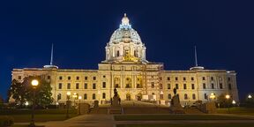 A wide white stone building photographed head-on at night. It rises in the center to a hemispherical central rotunda.