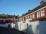 A series of red houses with dark roofs are partially hidden behind a white, deteriorating wall.