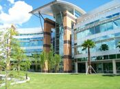 A modern architectural style building is seen clad in stone, metal, and glass against the backdrop of trees and a blue sky.