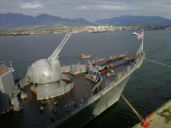 A close view of the AK-130 dual purpose guns on the bow with Vancouver's north shore in the background.