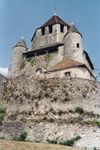 A grey stone castle rises above a stone retaining wall. The central, octagonal tower is flanked by two round towers.