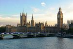 Neo-gothic Westminister palace and Big Ben clock tower stand above a river and bridge.