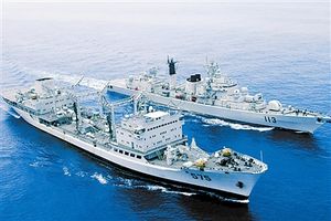 Starboard bow view of a guided-missile destroyer and naval auxiliary vessel seaming together in formation on a calm sea.