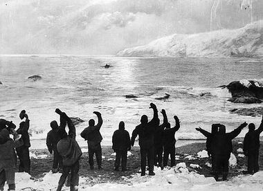 A black-and-white photograph of a group of men waving to something in the distance