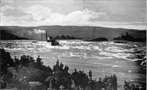 A river boat with more than a dozen windows along its visible side runs a set of rapids on a very large river. Smoke or steam rises from its smokestack and flows behind the boat parallel to the water. In the foreground, a crowd of 50 people watch the boat from the rocky shore.