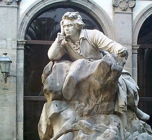 Statue of a man sitting on a rock, with an intent look.