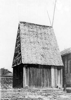 Large wooden rectangular house with steeply peaked roof in thatch