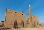 Temple ruins with several standing statues and an obelisk