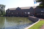 A large building stands behind a big pool of water, which enters the former through six gratings.