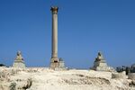 An ancient pillar and a sphinx statue among ruins