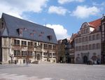 A town square with two visible buildings and a few tourists.