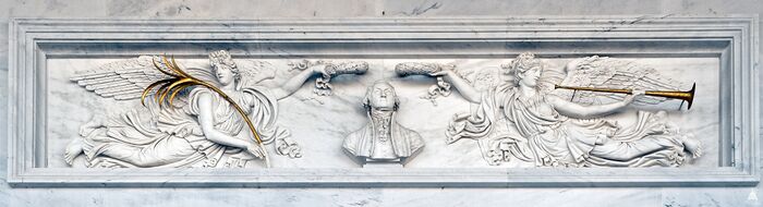 تمثال نصفي لـ جورج واشنطن محاطاً برمزي السلام التي تحمل غصن نخيل والشهرة تنفخ بوقاً، ونقشاً رخامياً (1959-1960) بواسطة جـ. جيانيتي (G. Gianetti) استناداً على الحجر الرملي (sandstone) من عام 1827 الأصلي بواسطة أنطونيو كابيلانو (Antonio Capellano)، في كابيتول الولايات المتحدة -الشهرة والسلام تتويج جورج واشنطن-