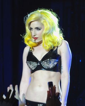 Left profile of a blond female wearing a black bustier with silver crystals on it. A head piece is attached to her left ear and the woman looks to the front.