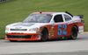 A red and white Chevrolet race car rounds a curve on a racing course.