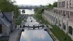 A small canal with a set of locks leading from a river near a large city.